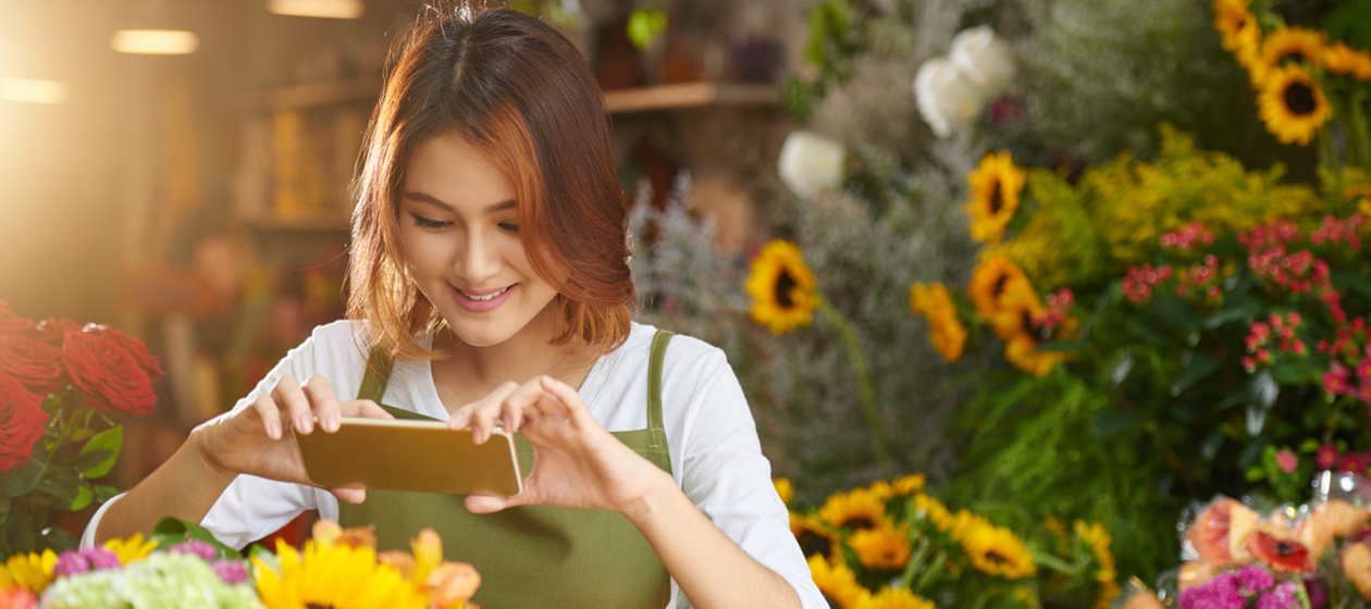 Frau mit Smartphone vor Blumenstrauß